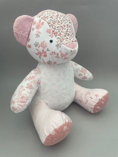 a pink and white teddy bear with flowers on it's head sitting against a gray background