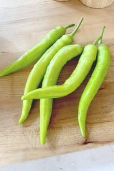 three green peppers sitting on top of a wooden cutting board