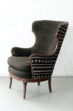 an upholstered chair sitting in front of a white brick wall with black accents