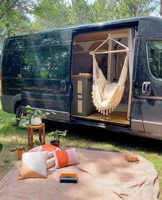 a black van with a hammock hanging from it's door and some pillows on the ground