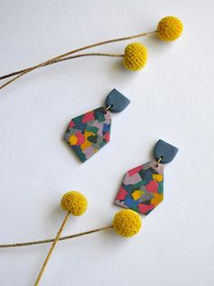 two earrings with yellow balls on top of them and one is made out of fabric