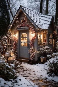 a small house covered in snow with christmas lights on the roof and wreaths around it