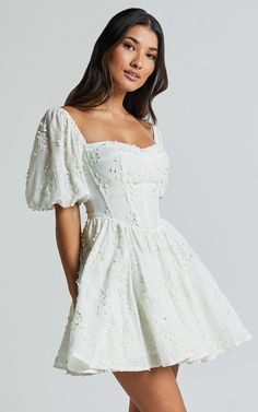 Celebrate the beauty of spring with our Esthela Mini Dress in Pale Mint. This enchanting piece features an embroidered square neck and short puff sleeves, giving it a sweet and feminine look. The corset detail cinches your waist for a flattering fit, while the flowy fit-and-flare silhouette adds a touch of romance to your outfit. Made from soft cotton fabric, this dress is perfect for both day-time parties and special occasions. Embrace your unique style and feel empowered in this gorgeous mini Ivory Outfit, Flowy Dress Short, Grad Dresses Short, Cotton Dress Fabric, White Dresses Graduation, Dresses For The Races, Short Puff Sleeve, Prom Dresses Modest, Formal Dresses Short