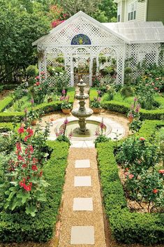 a garden with a fountain surrounded by flowers and trees in front of a white house