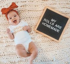 a baby laying on top of a blanket next to a chalkboard with the words my rolls are homemade