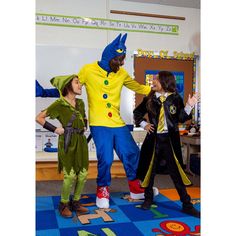 three children dressed up in costumes standing on a blue rug and smiling at each other