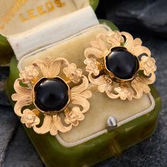 These bold earrings feature a round onyx cabochon at the center of an engraved floral openwork border. The earrings are crafted in 14k yellow gold and are finished with posts and friction backs for pierced ears. Evening Yellow Gold Cabochon Jewelry, Art Deco Clip-on Jewelry For Formal Occasions, Clip-on Art Deco Jewelry For Formal Occasions, Formal Art Deco Clip-on Jewelry, Elegant Yellow Gold Clip-on Earrings With Cabochon, Black Cabochon Earrings For Evening, Formal Yellow Gold Earrings With Black Enamel, Elegant Black Cabochon Earrings, Evening Black Cabochon Earrings