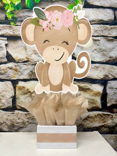 a paper cut out of a monkey with flowers on it's head, sitting in front of a brick wall