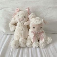 two white stuffed animals sitting on top of a bed next to each other with pink bows