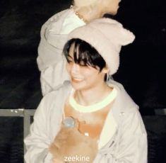 a woman holding a teddy bear while wearing a white coat and hat with the words zeeekine on it