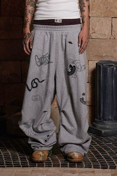 The Graffiti Crinkled Wide-Leg Sweatpants perfectly merge street style with a playful, artistic flair. These sweatpants are adorned with an all-over print of quirky graffiti graphics, adding a vibrant and dynamic touch to the design. The double-waist elastic band provides a unique and comfortable fit, while the crinkled texture along the legs enhances the visual appeal. The back features curved stitching for added dimension, making these pants as stylish as they are comfortable. Crafted from pre Casual Graphic Print Pants For Streetwear, Hip Hop Graphic Print Pants For Streetwear, Hip Hop Graphic Print Streetwear Pants, Baggy Graphic Print Bottoms For Streetwear, Baggy Streetwear Pants With Graphic Print, Urban Baggy Bottoms With Graphic Print, Baggy Graphic Print Pants For Streetwear, Baggy Hip Hop Pants With Graphic Print, Urban Pants With Graphic Print For Streetwear