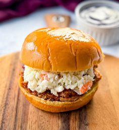 a pulled pork sandwich with coleslaw and mayonnaise on a wooden cutting board