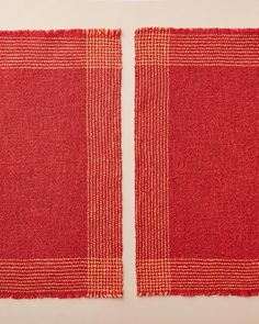 two pieces of red woven fabric on a white tablecloth with orange squares in the middle