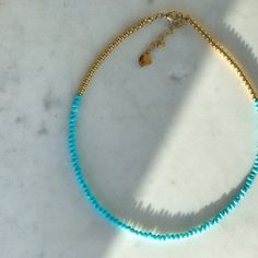 a blue beaded necklace on a marble surface with a gold chain and clasp closure