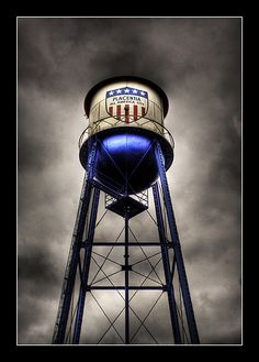 an old water tower with the american flag painted on it's side and dark clouds in the background