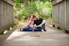 two young children sitting on a wooden bridge in the woods with their arms around each other