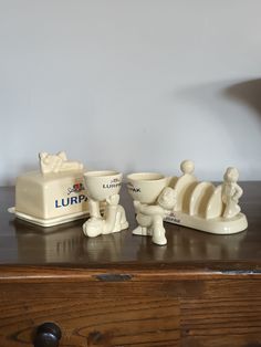 three ceramic figurines sitting on top of a wooden table next to a lamp