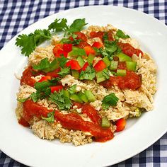 a white plate topped with rice covered in sauce and veggies on top of a checkered table cloth