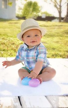 a baby sitting on the ground with a ball in it's hands and wearing a hat