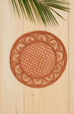 an oval woven placemat on a wooden surface with palm leaves in the foreground