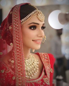 a woman wearing a red and gold bridal outfit with jewelry on her head, smiling at the camera