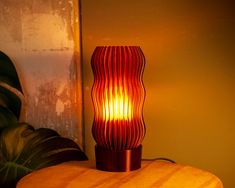 a red lamp sitting on top of a wooden table next to a green leafy plant