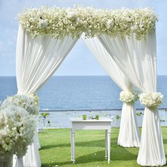 an outdoor wedding setup with white flowers and draping on the grass by the ocean