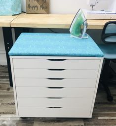 an ironing board sitting on top of a white filing cabinet next to a blue chair