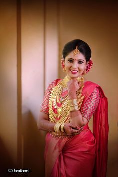 a woman in a red sari and gold jewelry posing for the camera with her hands on her chest