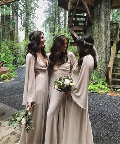 three bridesmaids are standing together in front of a wooden structure and trees, one is holding her bouquet