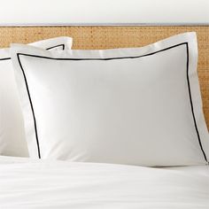 a bed with white sheets and black piping on the pillowcase, next to a headboard