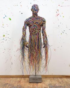 a sculpture made out of multicolored threads in front of a white wall