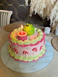 there is a cake with two candles on it and one has a green frog sitting in the middle