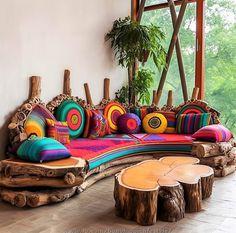 a couch made out of wooden logs with colorful pillows on the top and bottom, sitting in front of a window