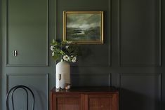 a vase with flowers sitting on top of a wooden cabinet next to a painting hanging on the wall