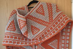 an orange and white crocheted blanket hanging on a door frame with a wooden hanger