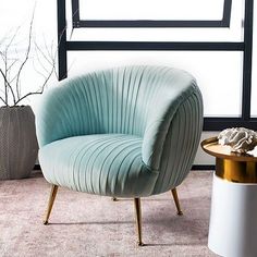 a blue chair sitting on top of a rug next to a white vase and gold table