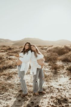 two women standing in the desert with their arms around each other and one woman holding her belly