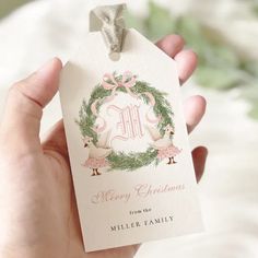 a hand holding a christmas gift tag with a monogrammed wreath on the front