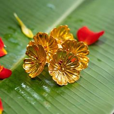 three gold flower brooches sitting on top of a green leaf next to red flowers