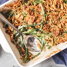 a casserole dish filled with green beans and fried onions, topped with a spoon