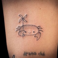 a small crab tattoo on the back of a woman's shoulder, with words written below it