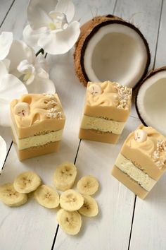 three slices of cake with bananas and coconuts around it on a white wooden table