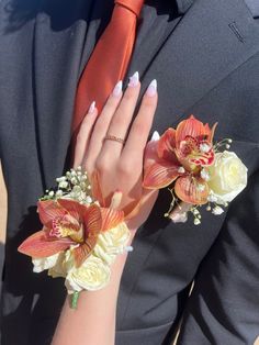 a woman in a suit and tie with flowers on her wrist, wearing an orange tie