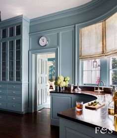 a kitchen with blue walls and wooden floors has a clock on the wall above the sink