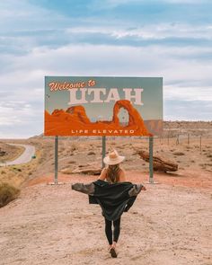 a woman walking down a dirt road in front of a welcome to utah sign