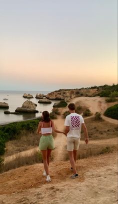 two people walking down a dirt path towards the ocean