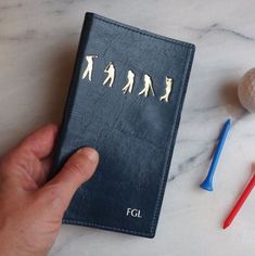 a person is holding a small book with golf pins and balls on the table next to it