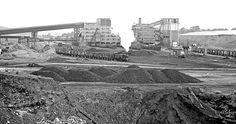 black and white photograph of an industrial area with large piles of dirt in the foreground