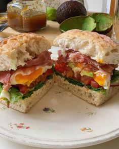 a sandwich cut in half sitting on top of a white plate next to avocado